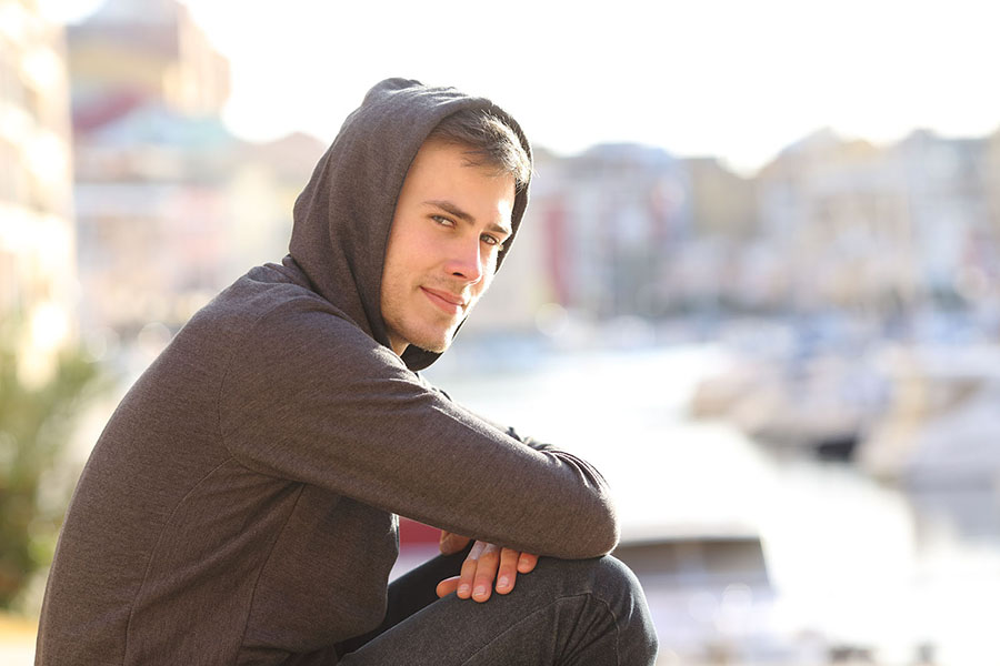 An optimistic teenager in a grey hoody looks at the camera with arms rested on knees
