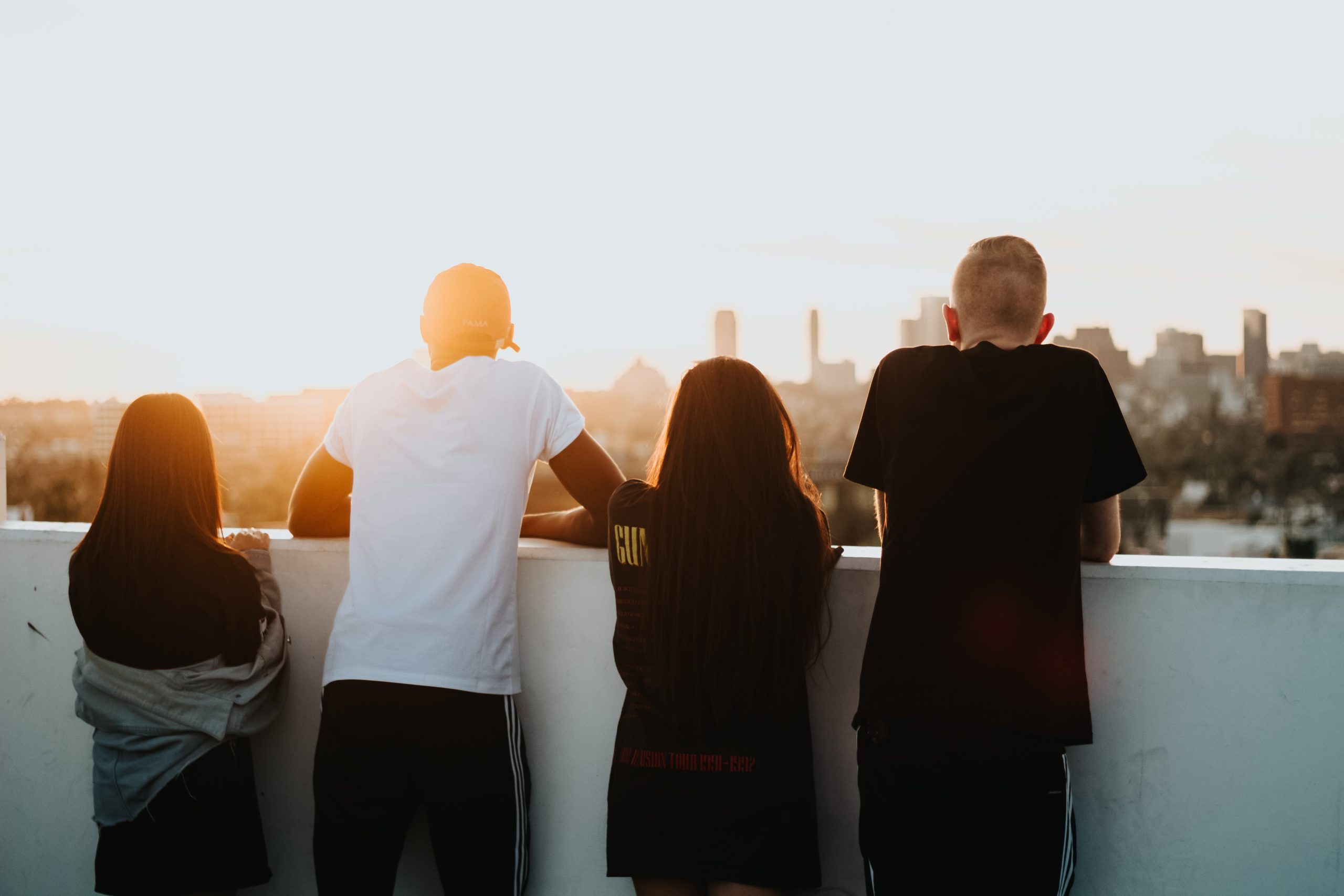 Four youth lean on a balcony to watch a sunset