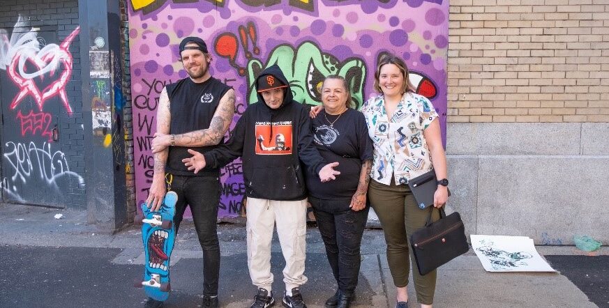 Dr Sofia Bartlett and community members in front of a mural in Vancouver