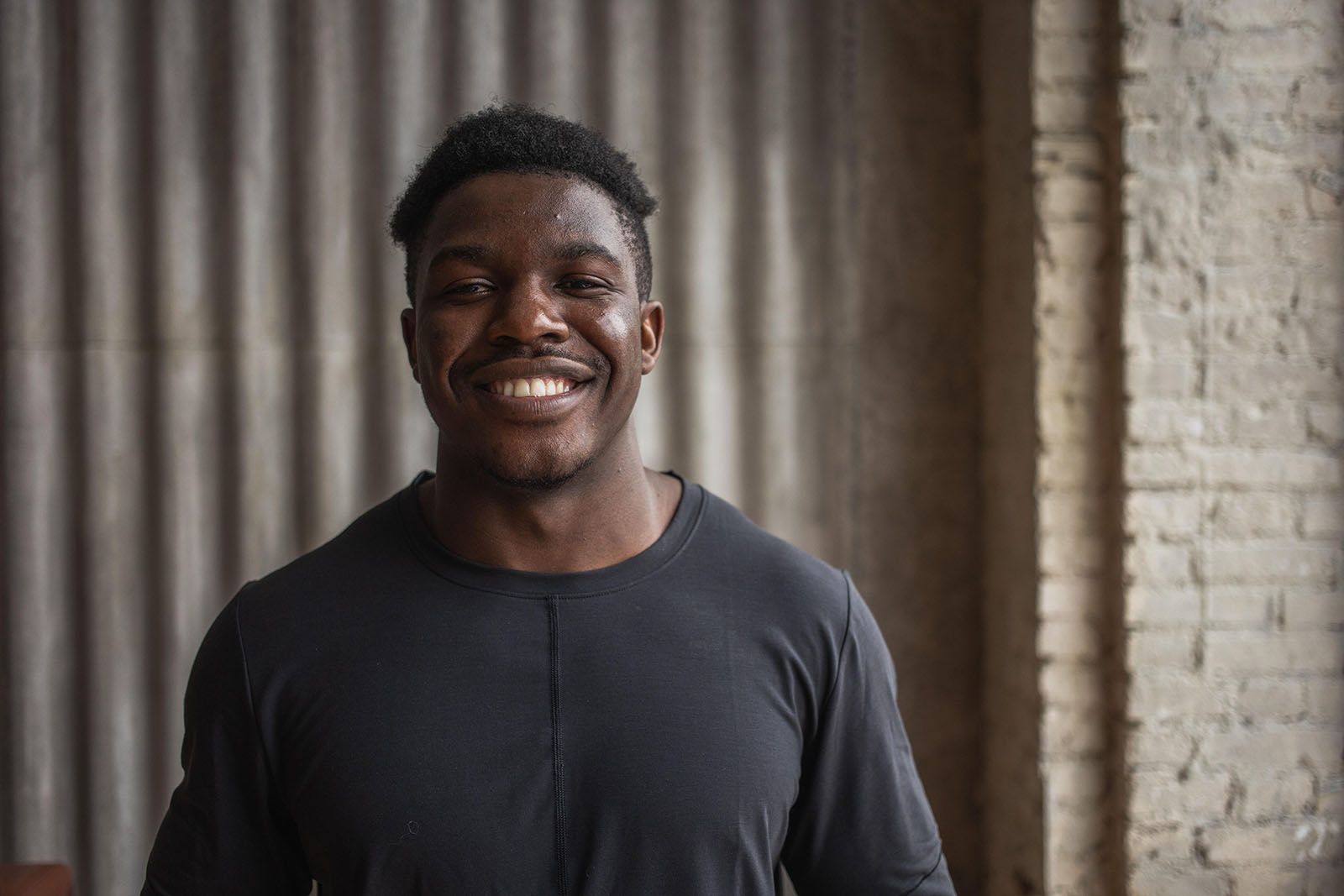 A man smiles at the camera in a grey shirt