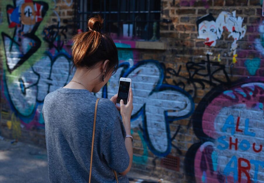 A woman looks at her phone in front of a graffiti covered wall