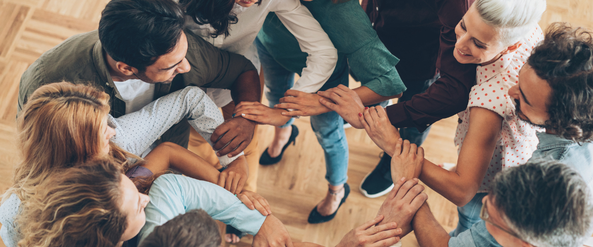 A group of friends stand in a circle creating a circular link with their forearms