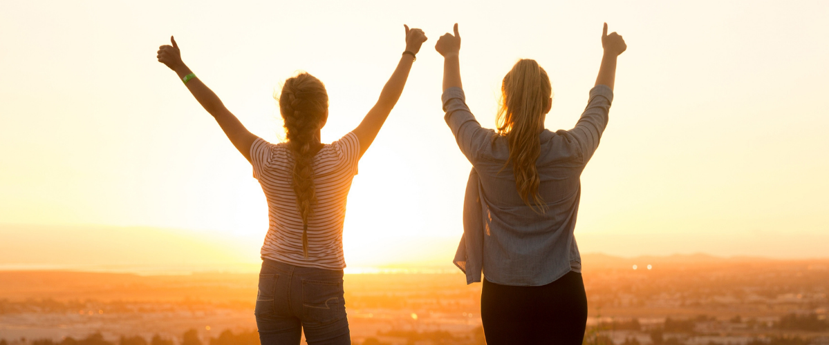 Two people face the sunset with their arms in the air