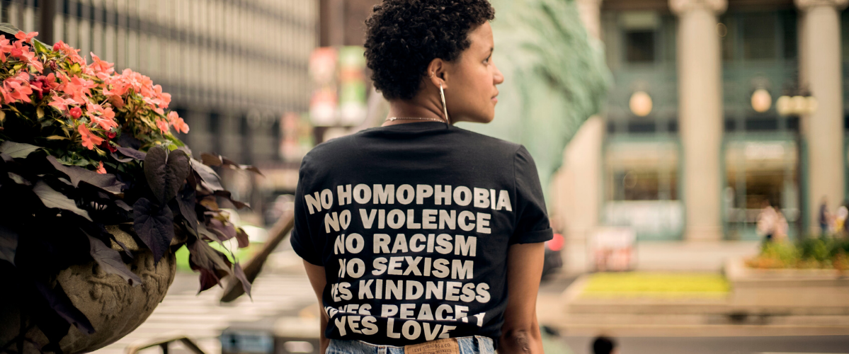 a woman wearing a shirt saying "no homophobia, violence, racism, sexism"