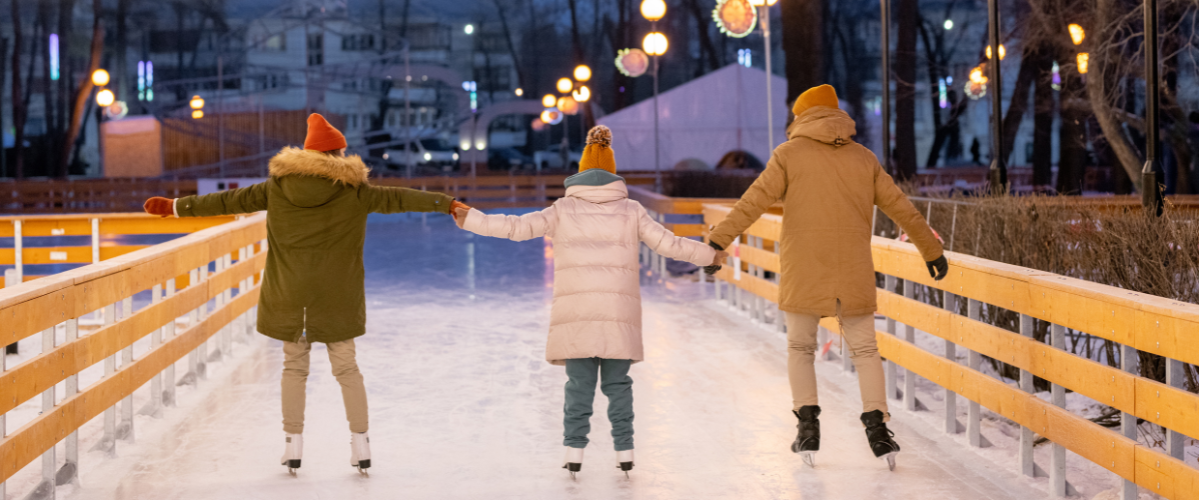 A family of three holds hands while ice skating outside at night