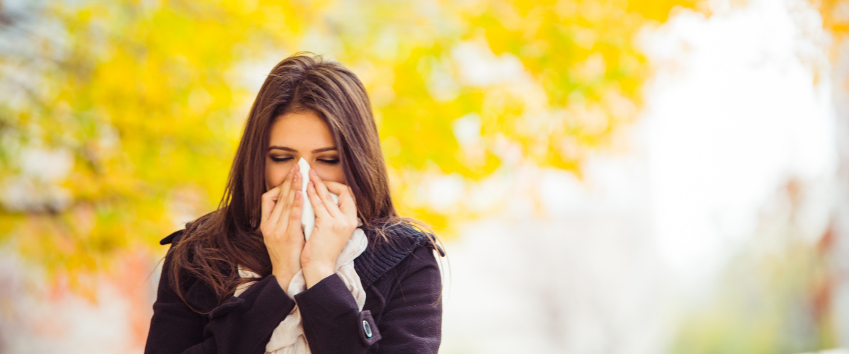 A woman walking outside during fall sneezing into a tissue
