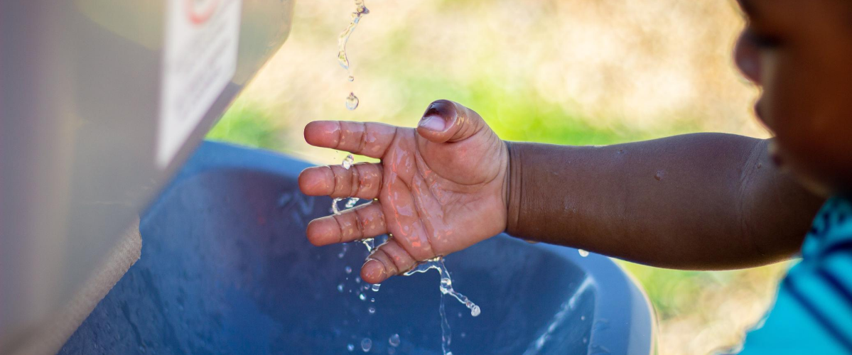 a little boy puts his hand out under running water