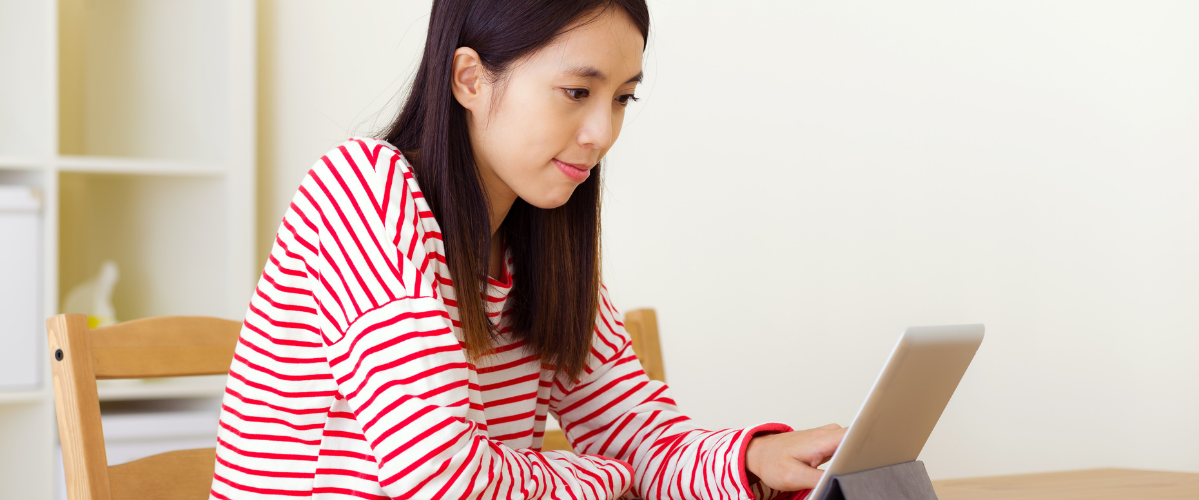 A woman sitting inside wearing a striped shirt reads something on a tablet