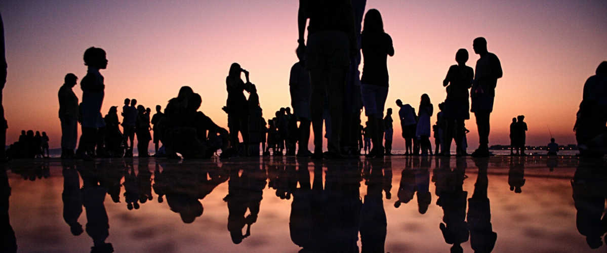 a large group of people and their silhouettes stand near the water after the sunset