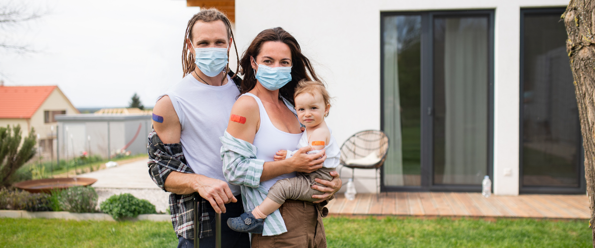 A couple hold their infant in their arms wearing masks after having received a vaccine